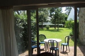 A patio with a table and chairs, a view of a garden with trees and a lawn. - Apartment in charming granite residence by the sea (Carnac)