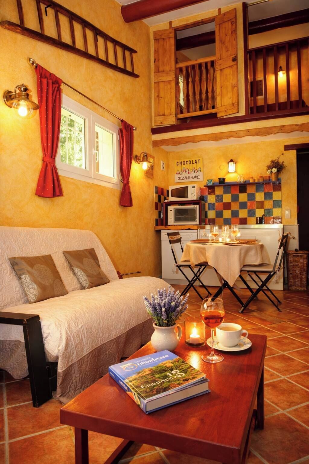 Une pièce chaleureuse avec un lit, une table à manger éclairée par une bougie, un livre et un panneau accroché au mur.