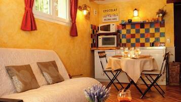 Une pièce chaleureuse avec un lit, une table à manger éclairée par une bougie, un livre et un panneau accroché au mur.
