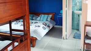 Een slaapkamer met een stapelbed, een eenpersoonsbed met bloemenbeddengoed, een nachtkastje, een spiegel, en een badkamer met een wastafel en spiegel.