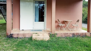 Een overdekte veranda met een witte deur, twee klapstoelen en een klein tafeltje.
