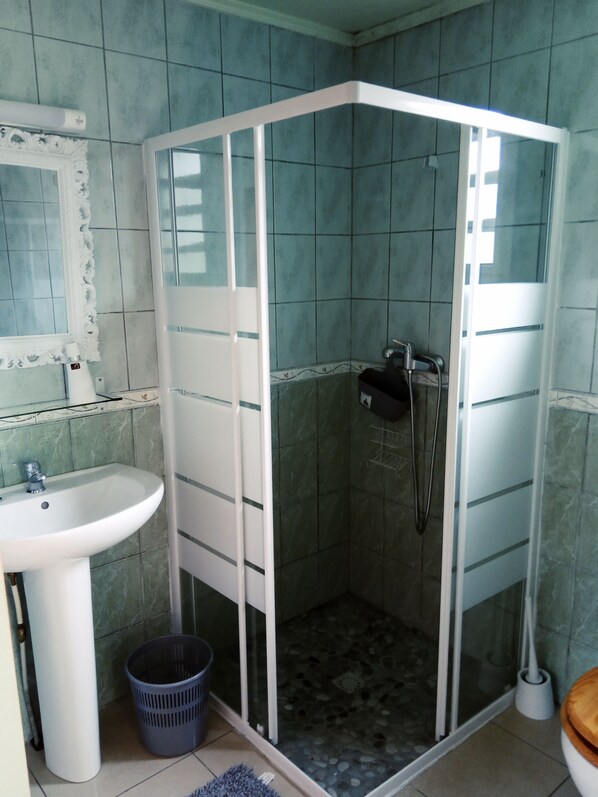 Un baño con ducha en esquina, lavamanos y espejo.