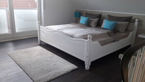 Une chambre avec un lit blanc, un tapis gris et une vue sur l’extérieur, visible à travers une porte vitrée.
