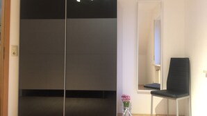 Una habitación con un amplio ventanal corredero, una silla, un espejo y un florero con flores.