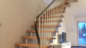 Una escalera moderna con escalones de madera y barandilla de metal, que conduce a una plataforma con superficie plana y un televisor.