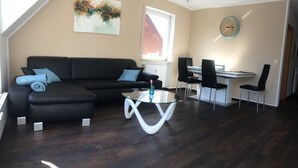 Una sala de estar moderna con un sofá negro, una mesa de centro de cristal y un comedor con una mesa blanca y sillas negras.