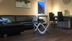 Una sala moderna con un sofá de cuero negro, una mesa de centro de vidrio y una zona de comedor con dos sillas negras.