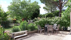 Un espace extérieur aménagé en terrasse, avec une table et des chaises, entouré d’une clôture et agrémenté de différentes plantes.