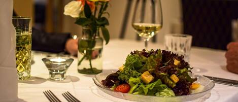 A dining table with a salad, wine glasses, and a candle.