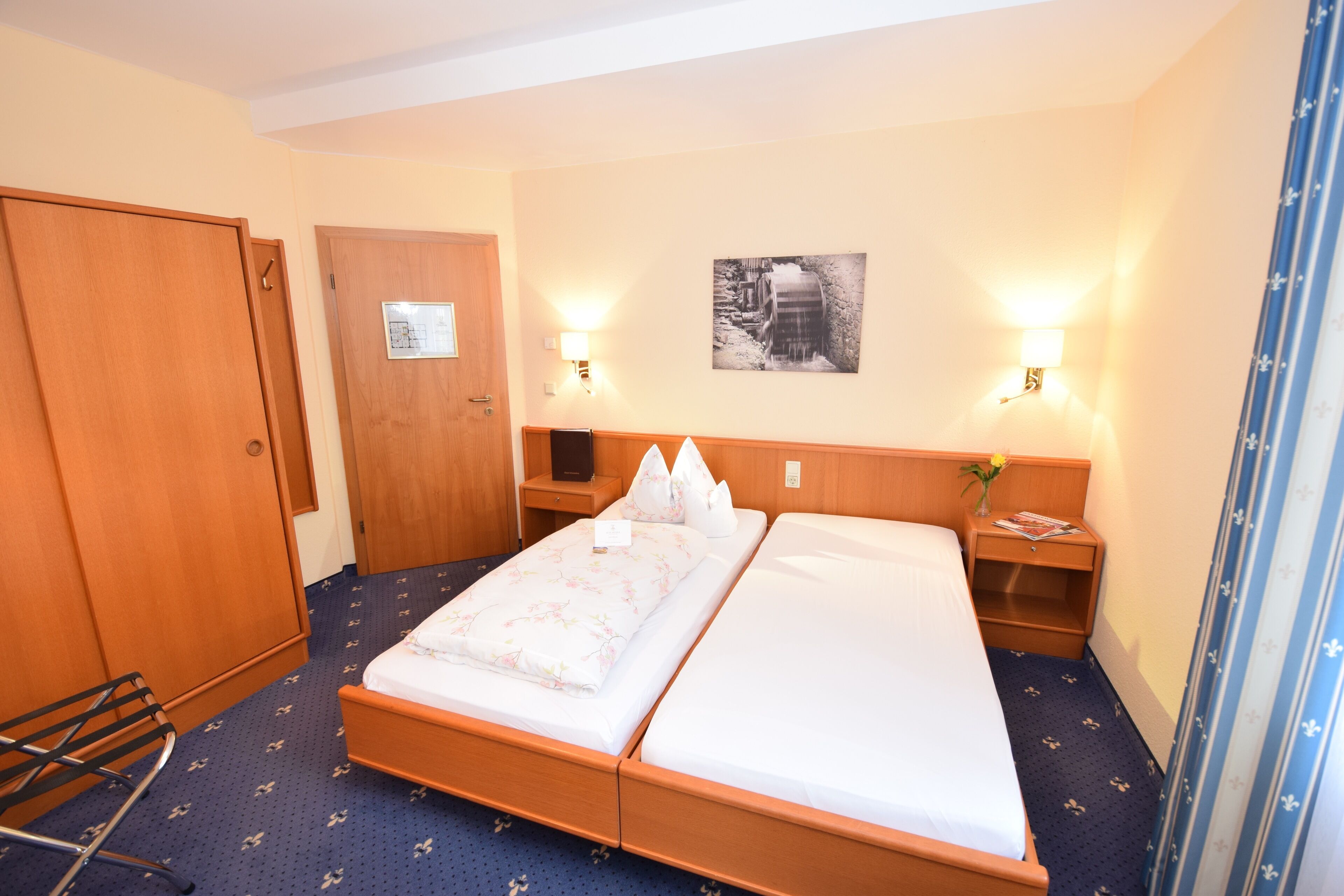 Una camera d'albergo con un letto matrimoniale, due comodini, un armadio in legno e un quadro appeso al muro.