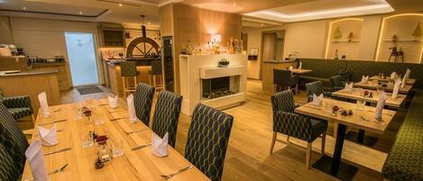 Un comedor moderno con mesas de madera y sillas tapizadas en verde, una chimenea y una zona de bar con mostrador de madera.