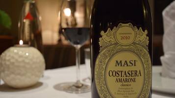 A bottle of Masi Costasera Amarone wine with a detailed label, placed on a table with a glass of red wine and a decorative object in the background.