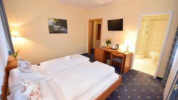 A hotel room with two beds, a desk, a TV, and a bathroom visible through an open door.