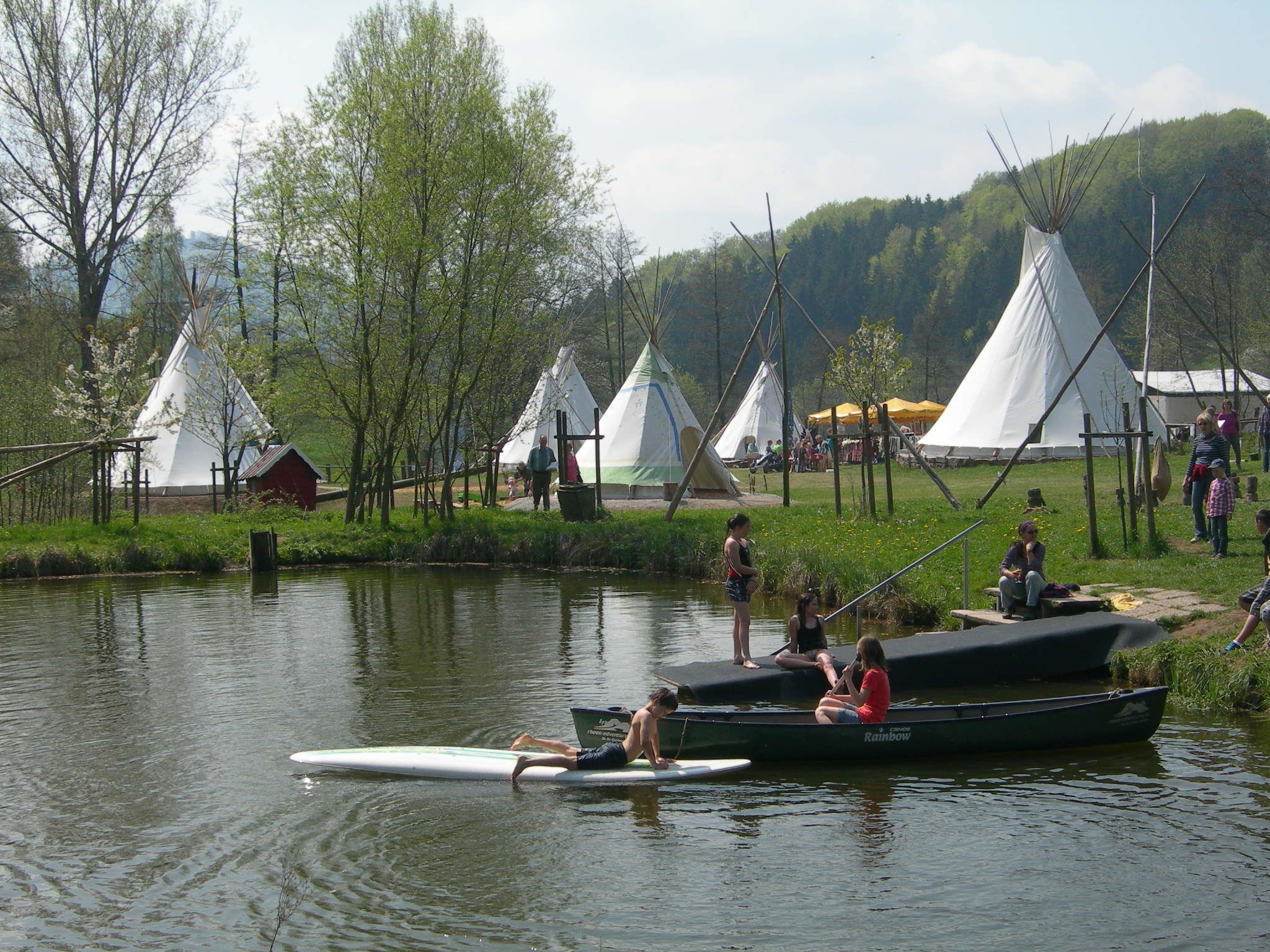 A lakeside campsite with teepees and a boat docked near the water.