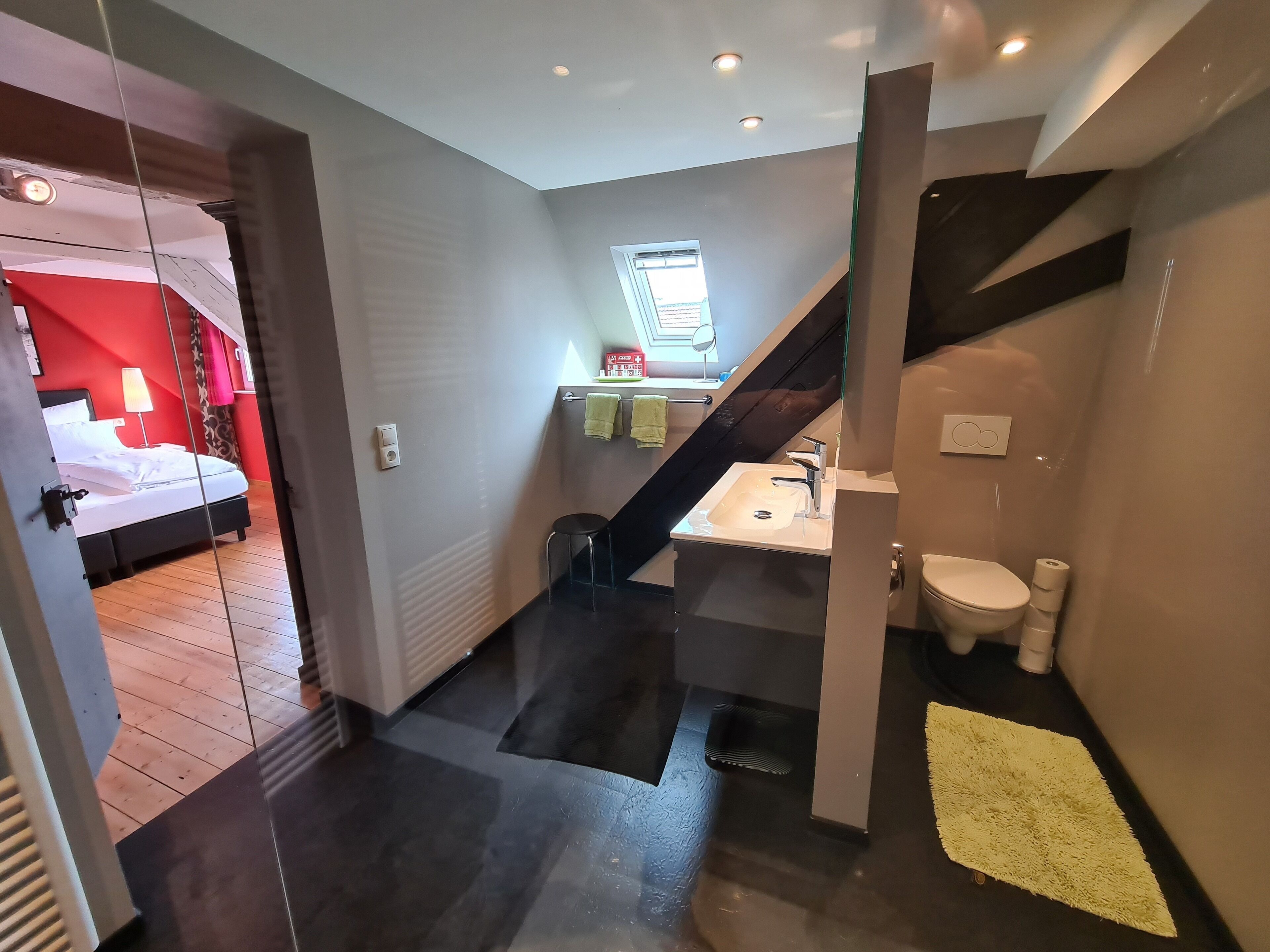 A modern bathroom with a sink, toilet, and a small stool. There is a staircase leading to another room.
