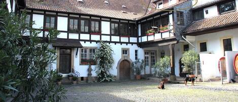 Un bâtiment traditionnel à colombages, doté d’une cour, où l’on voit un chien et une personne qui se promène.
