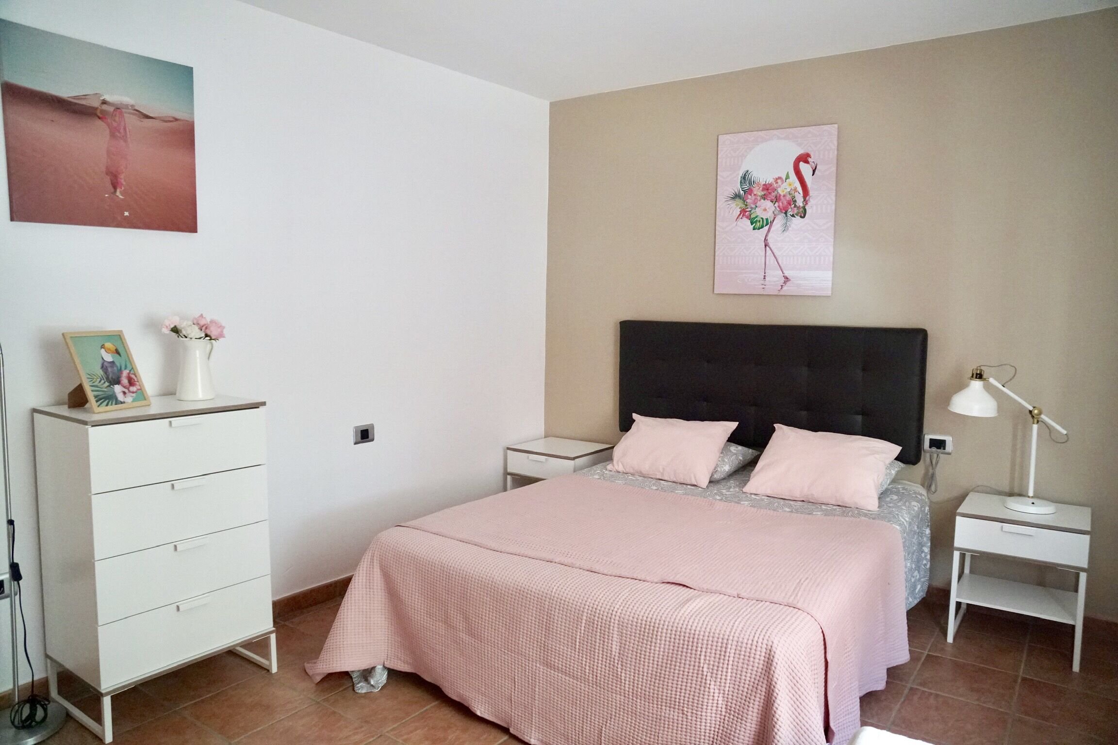 A bedroom with a bed, a dresser, a nightstand, a lamp, and two wall art pieces.