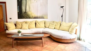 A living room with a curved sofa, a coffee table, and a painting of a forest. - Playa San Juan, a large apartment with 3 bedrooms, for families, group  (Playa San Juan)