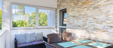 A sunlit patio with a stone wall, a cushioned bench, and a wooden table with blue placemats.