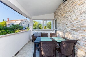 Uma varanda com mesa e cadeiras, um muro de pedra e vista para edifícios e vegetação.