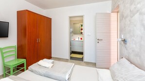 A bedroom with a bed, a green chair, a wooden wardrobe, and a bathroom visible through an open door.