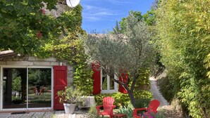 Un jardín con sillas rojas, una planta en maceta y un muro de piedra.
