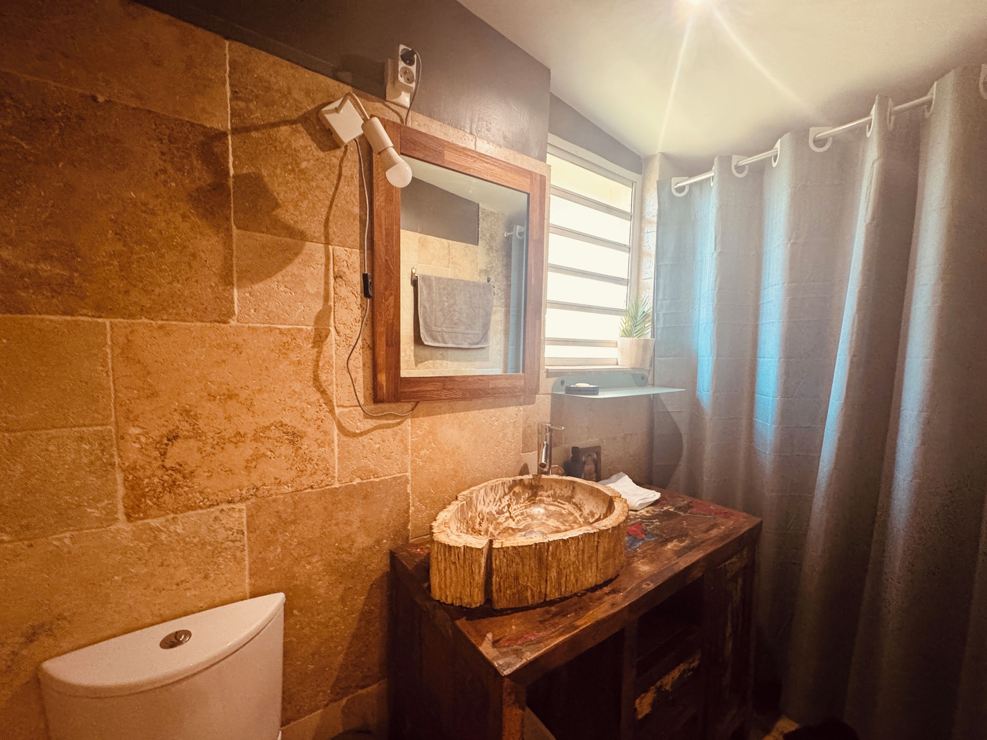Une salle de bain avec des murs en pierre, un meuble-lavabo en bois, un miroir, un porte-serviettes et une fenêtre avec des rideaux.