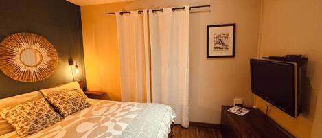 Un dormitorio con cama, televisor, aire acondicionado de pared y un cuadro enmarcado.