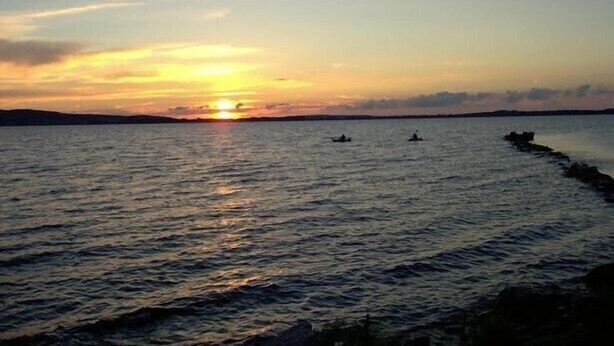 Un atardecer sobre una superficie acuática tranquila con barcos.