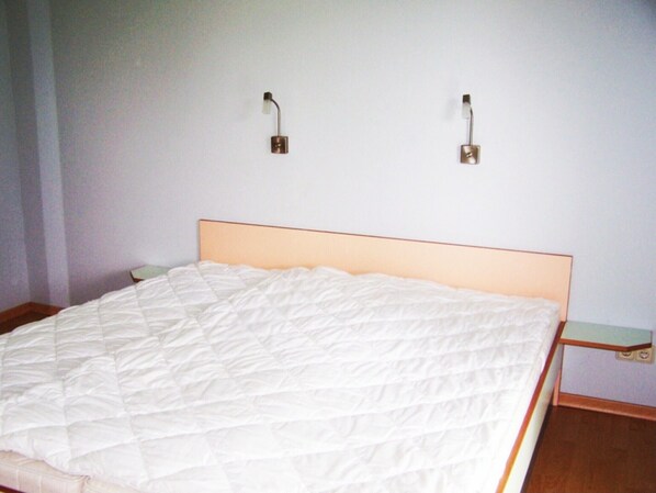 A bed with a white quilted cover, a wooden headboard, and two wall-mounted light fixtures.