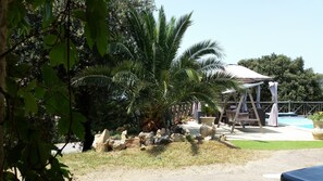 Un jardín tropical con palmeras, un conjunto de columpios y una zona de piscina.