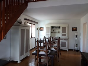Un comedor con sillas de madera y una mesa, una escalera y un armario blanco con estantes.