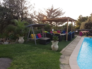 Un patio trasero con piscina, mobiliario de exterior y un columpio.