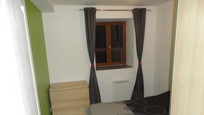 A bedroom with a bed, a window with curtains, a radiator, and a green wall.