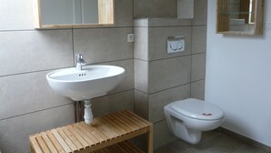 A bathroom with a white sink, wooden shelf, and a toilet.