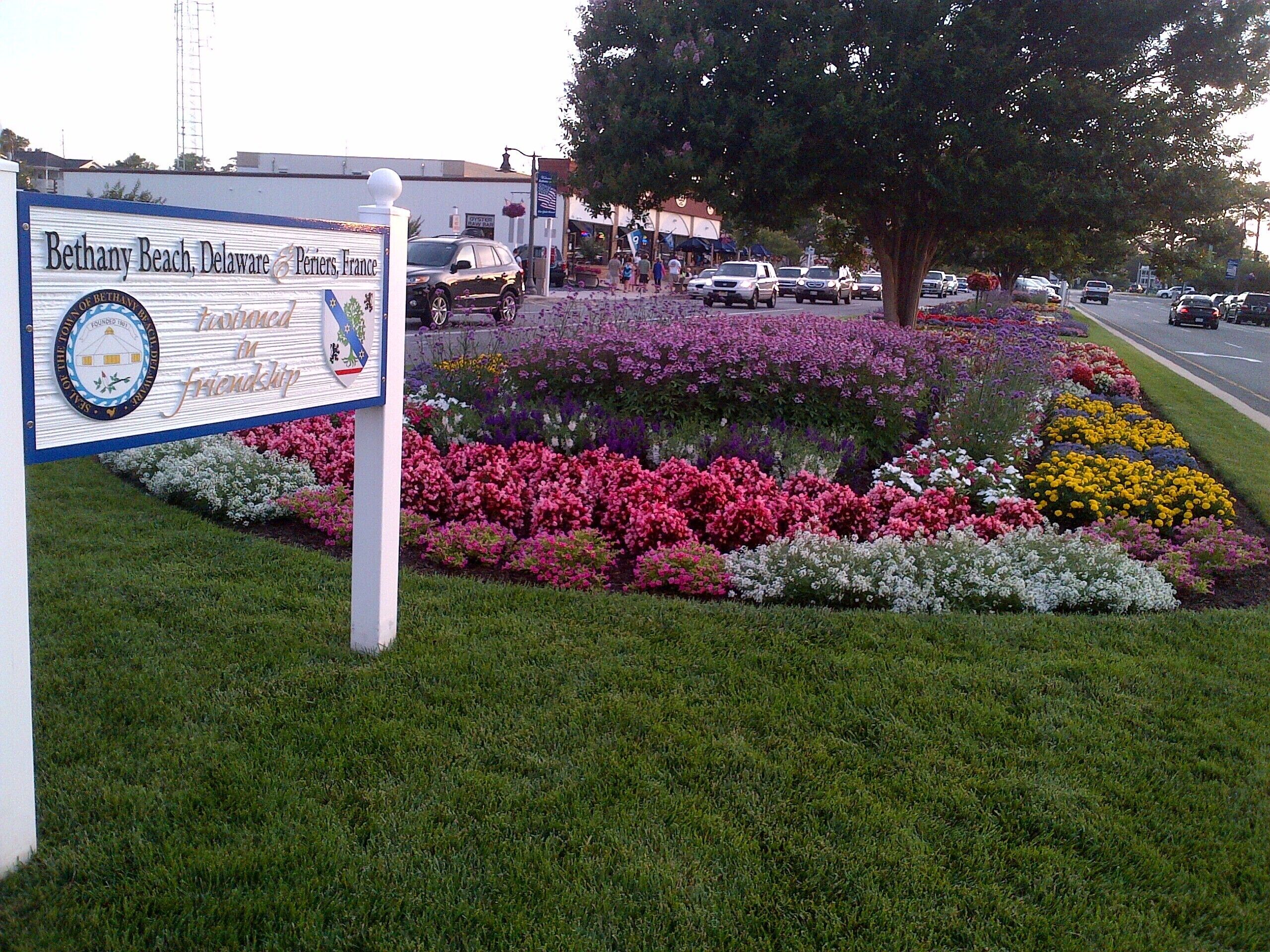 A sign for Bethany Beach, Delaware & Penns, France, with a flower garden in front.