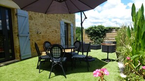 Une terrasse extérieure avec une table et des chaises, un grand parasol et un mur en pierre.