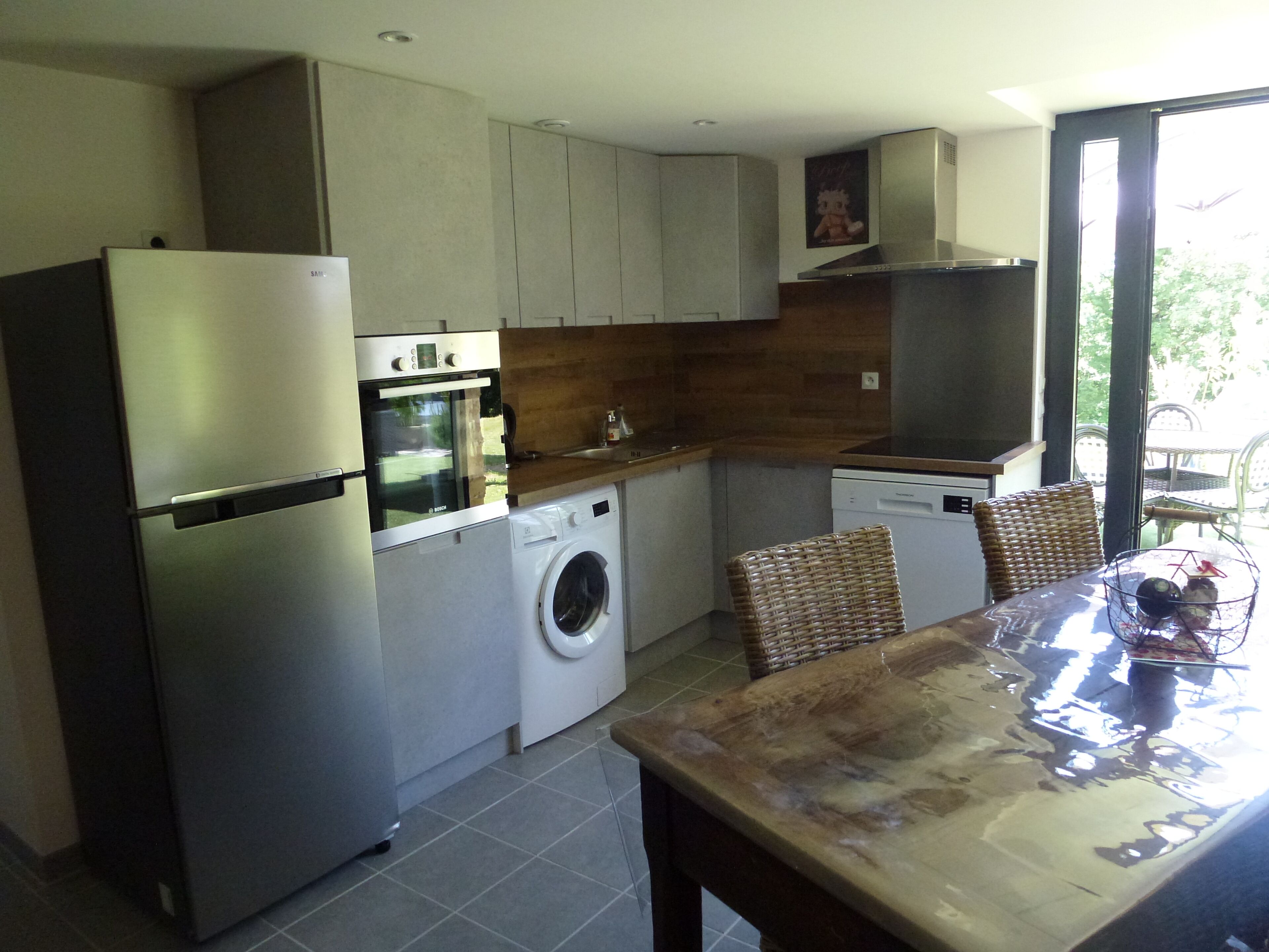 Een functionele keuken met een inbouwoven, wasmachine en een eethoek met tafel en stoelen.