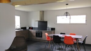 A modern kitchen with a dining area, featuring a built-in oven, a range hood, and a large window providing natural light.