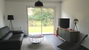 A modern living room with a sofa, a coffee table, a TV on a wooden cabinet, a floor lamp, and a chair.