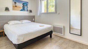 A bedroom with a bed, a window, a radiator, a wall-mounted lamp, and a painting.