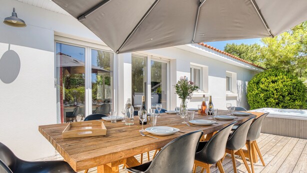 An outdoor dining area with a wooden table, black chairs, and a large umbrella.