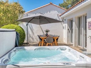 A hot tub with a table and chairs under an umbrella, a patio area, and a building with a tiled roof. - Villa Maroc - Domaine Le Sherwood (Notre-Dame-De-Monts)