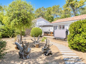 Ein Haus mit Terrasse, überdachter Sitzgelegenheit und Garten mit Bäumen und Sträuchern.