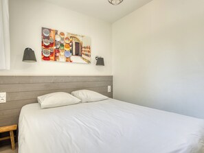 Ein Schlafzimmer mit hölzernem Kopfteil, einem Bett mit weißer Bettwäsche, zwei Wandlampen und einem farbenfrohen Wandbild.