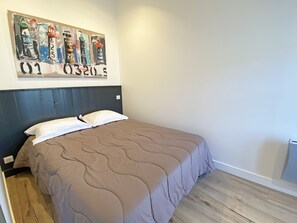 Une chambre à coucher comprenant un lit, une tête de lit, une œuvre d’art accrochée au mur et un radiateur.