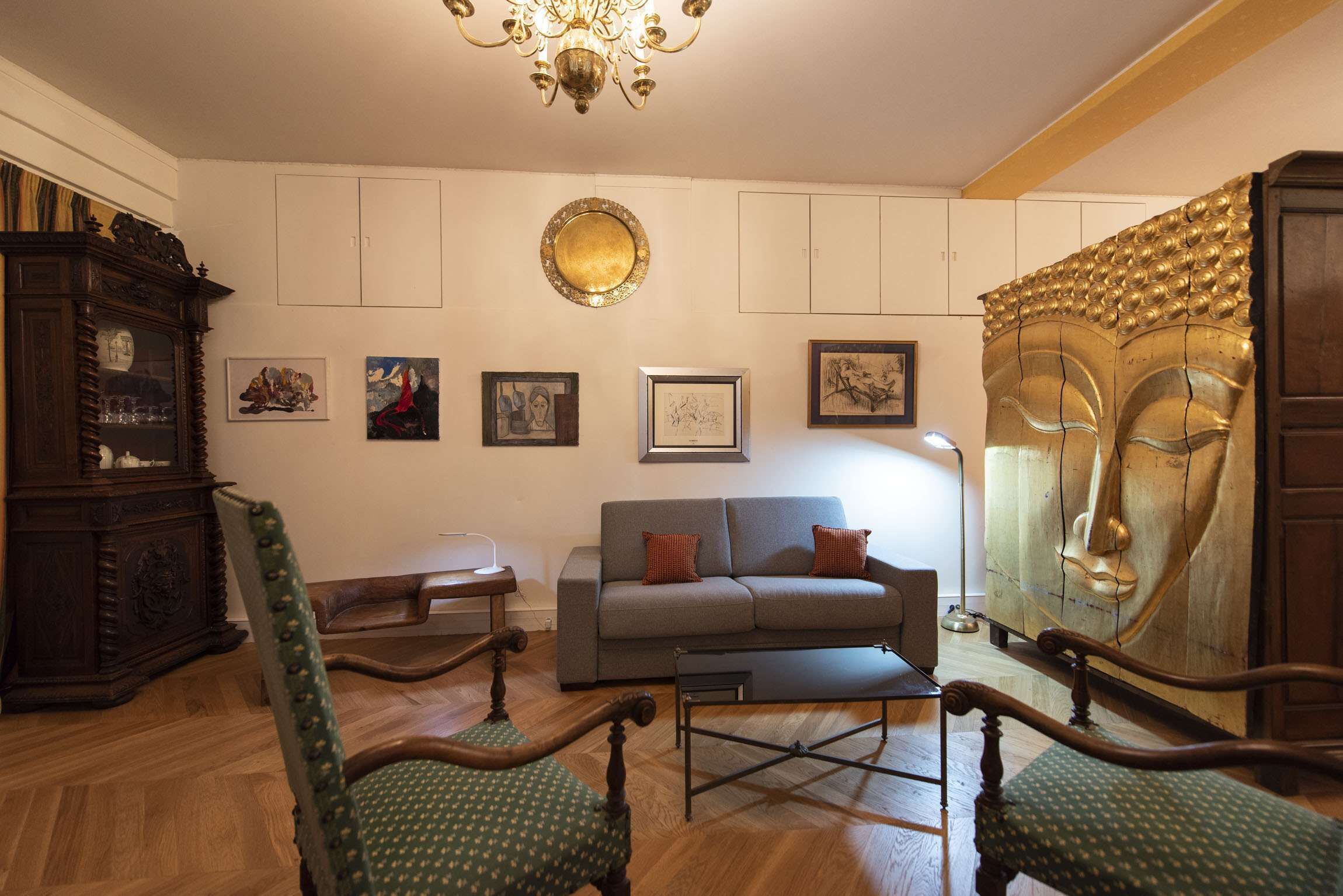 Una sala de estar con sofá, dos sillones, un aparador de madera y una araña.