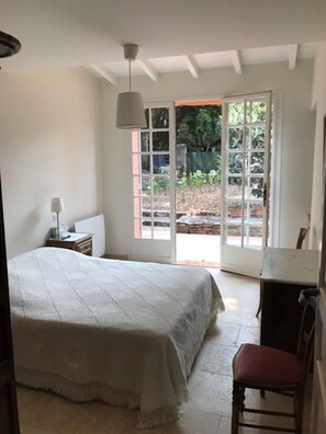 A bedroom with a bed, a desk, a chair, and a window with a view of the garden. - Completely renovated house (Oppède)