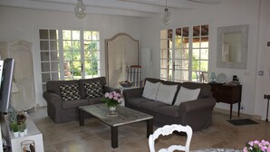 Ein geräumiges Wohnzimmer mit zwei Sofas, einem Couchtisch und einem Fernseher. Große Fenster sorgen für natürliches Licht und einen Blick ins Grüne.