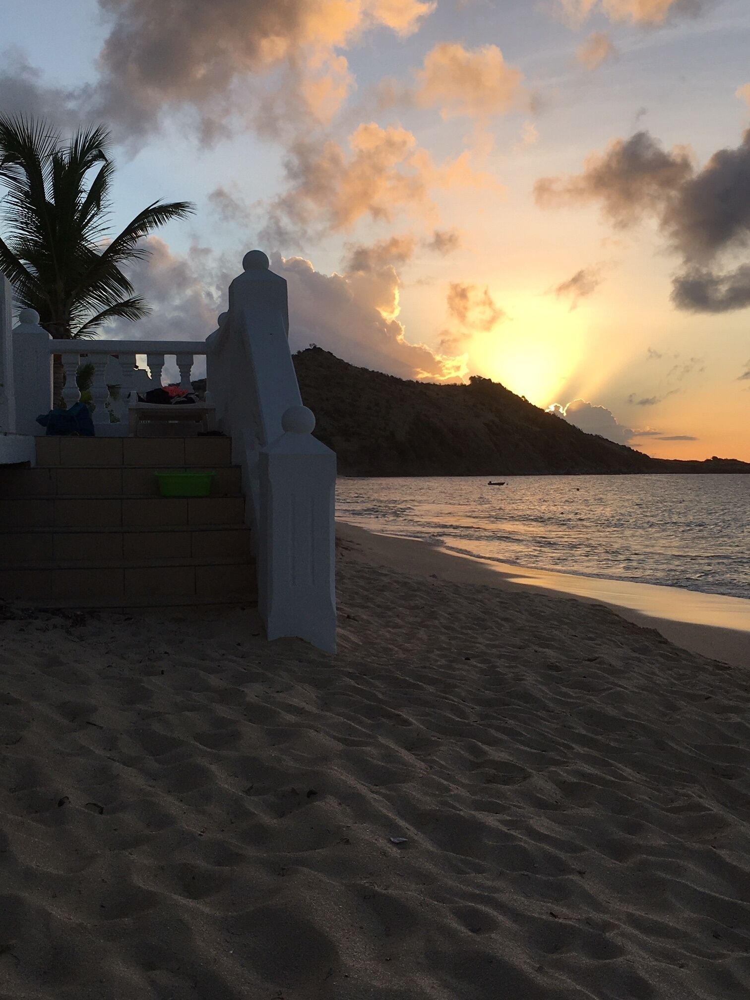 A beach with a white building, palm trees, and a sunset.